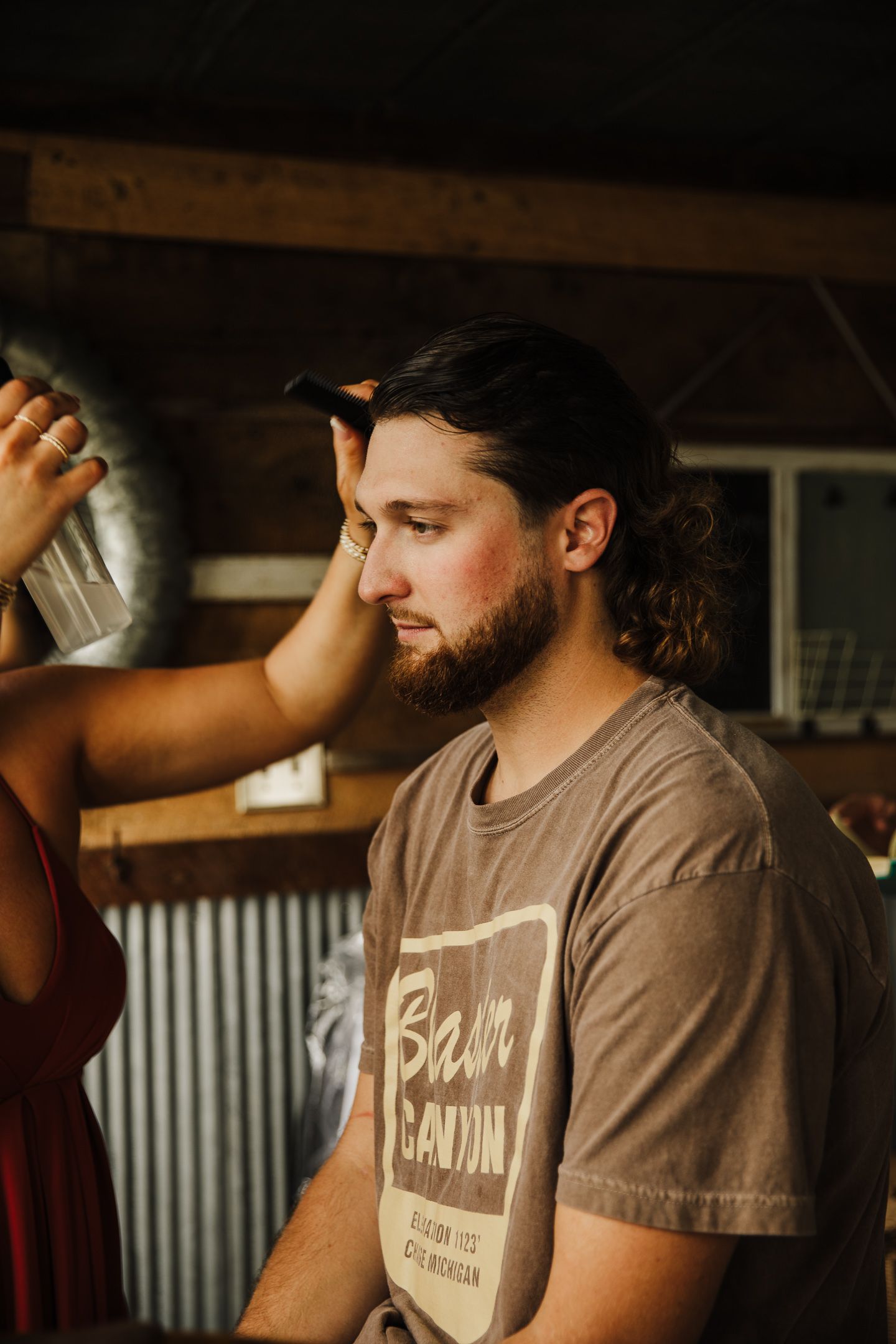 Man in brown t-shirt with barn logo photographed in rustic setting.