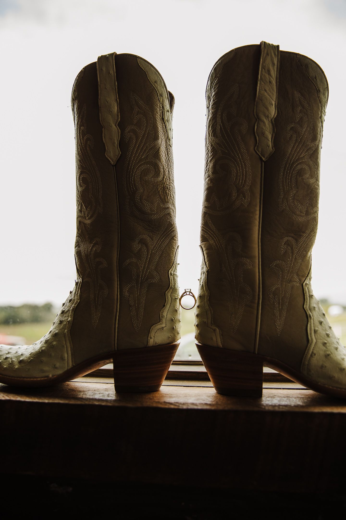 Silhouetted cowboy boots lined up on window ledge with backlit dramatic lighting.