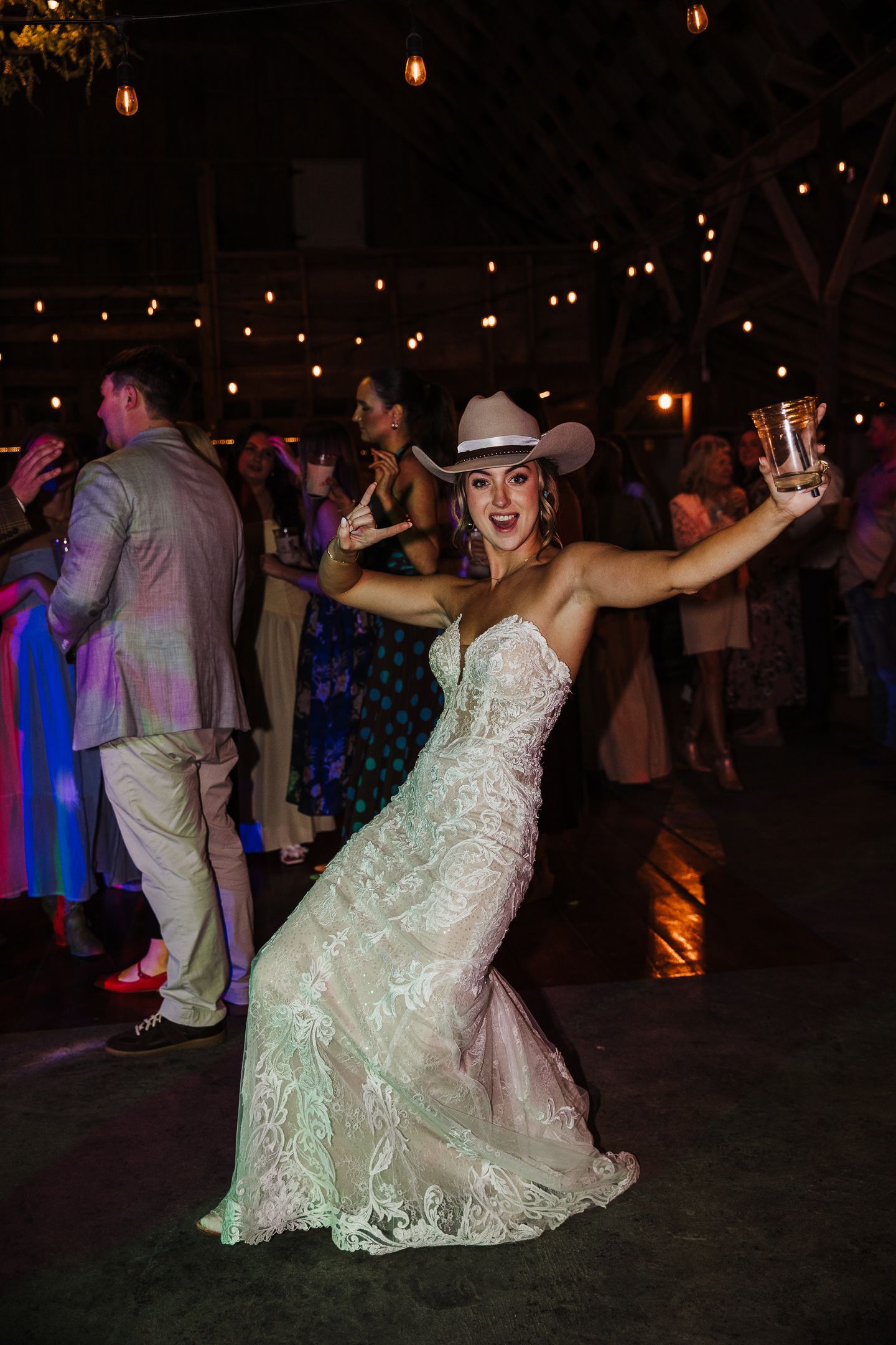 Bride in lace gown dances joyfully under string lights at evening reception.
