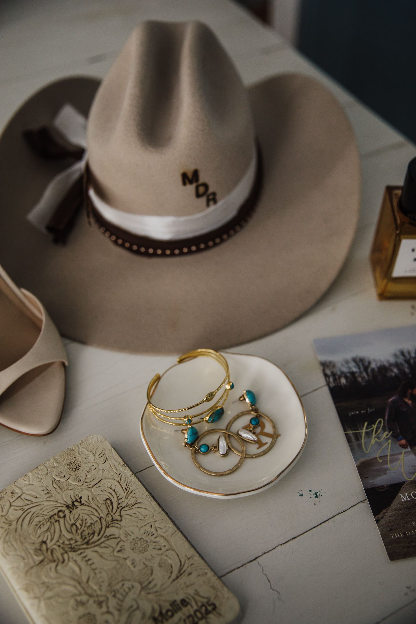 Rustic western cowboy hat and delicate turquoise jewelry displayed on a textured surface with decorative designs.