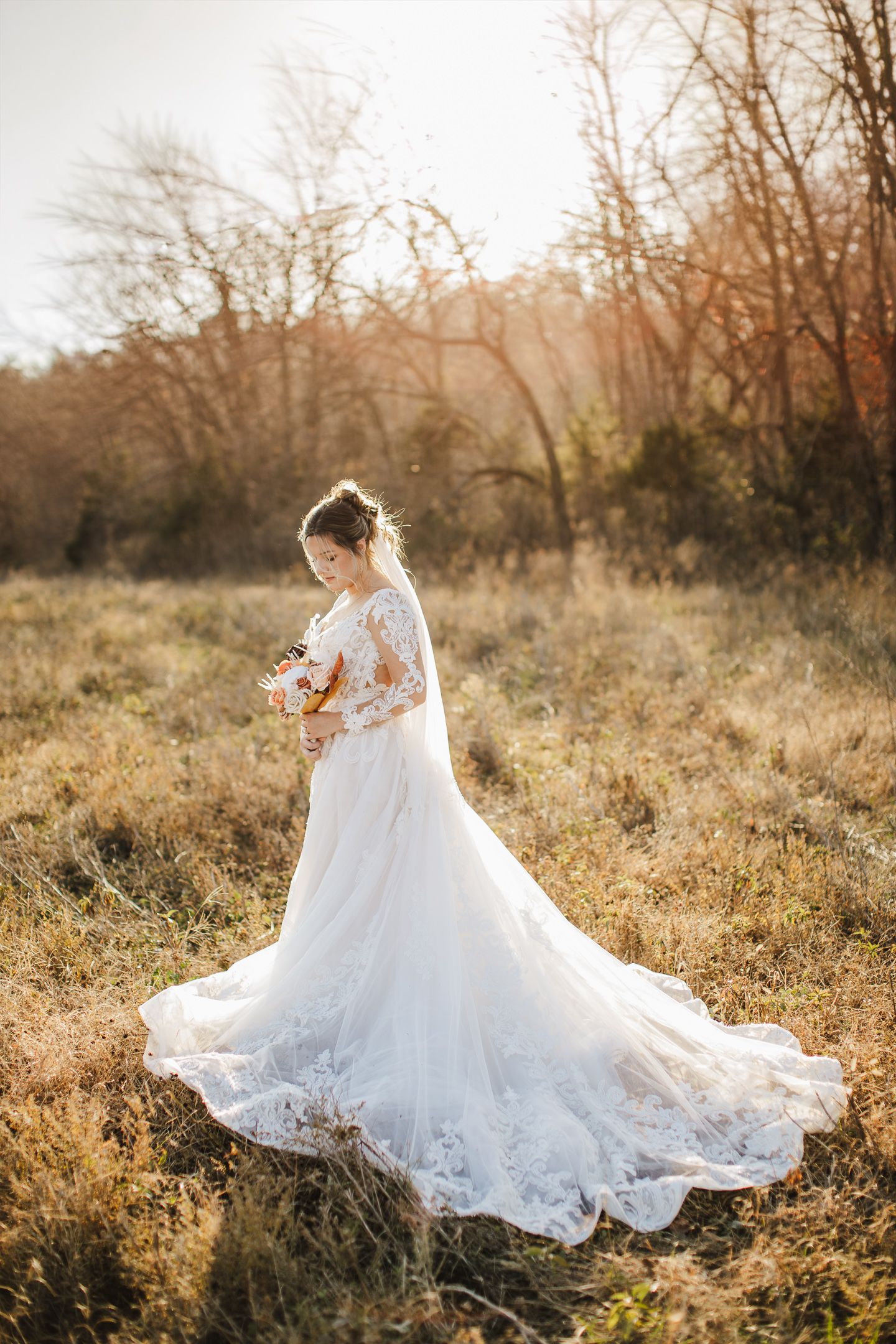 Stunning bridal portraits showing the dramatic flow of a lace wedding gown in golden sunlit field.
