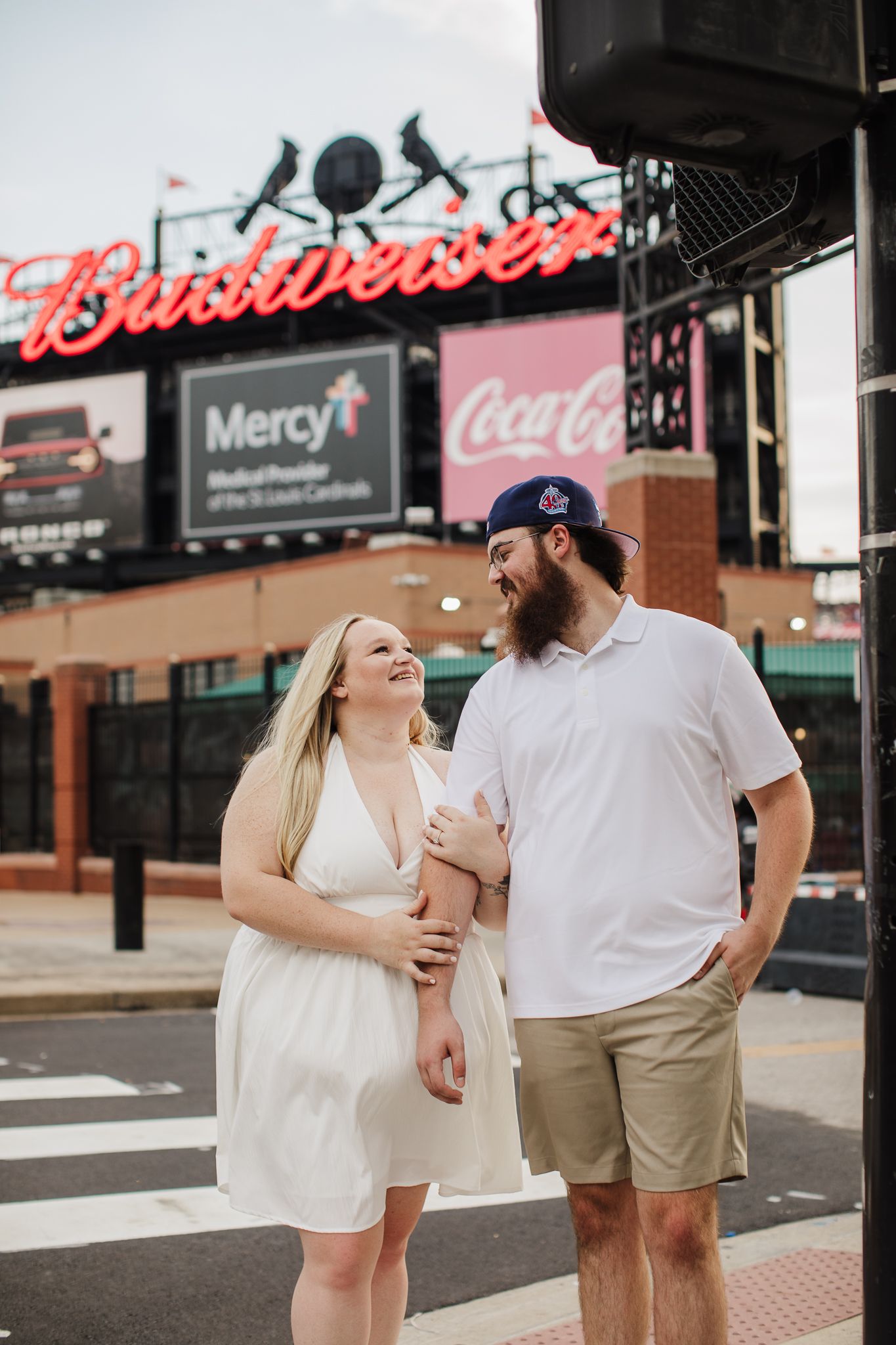 Couple walking together near a stadium with Budweiser and Coca-Cola signs visible in background.