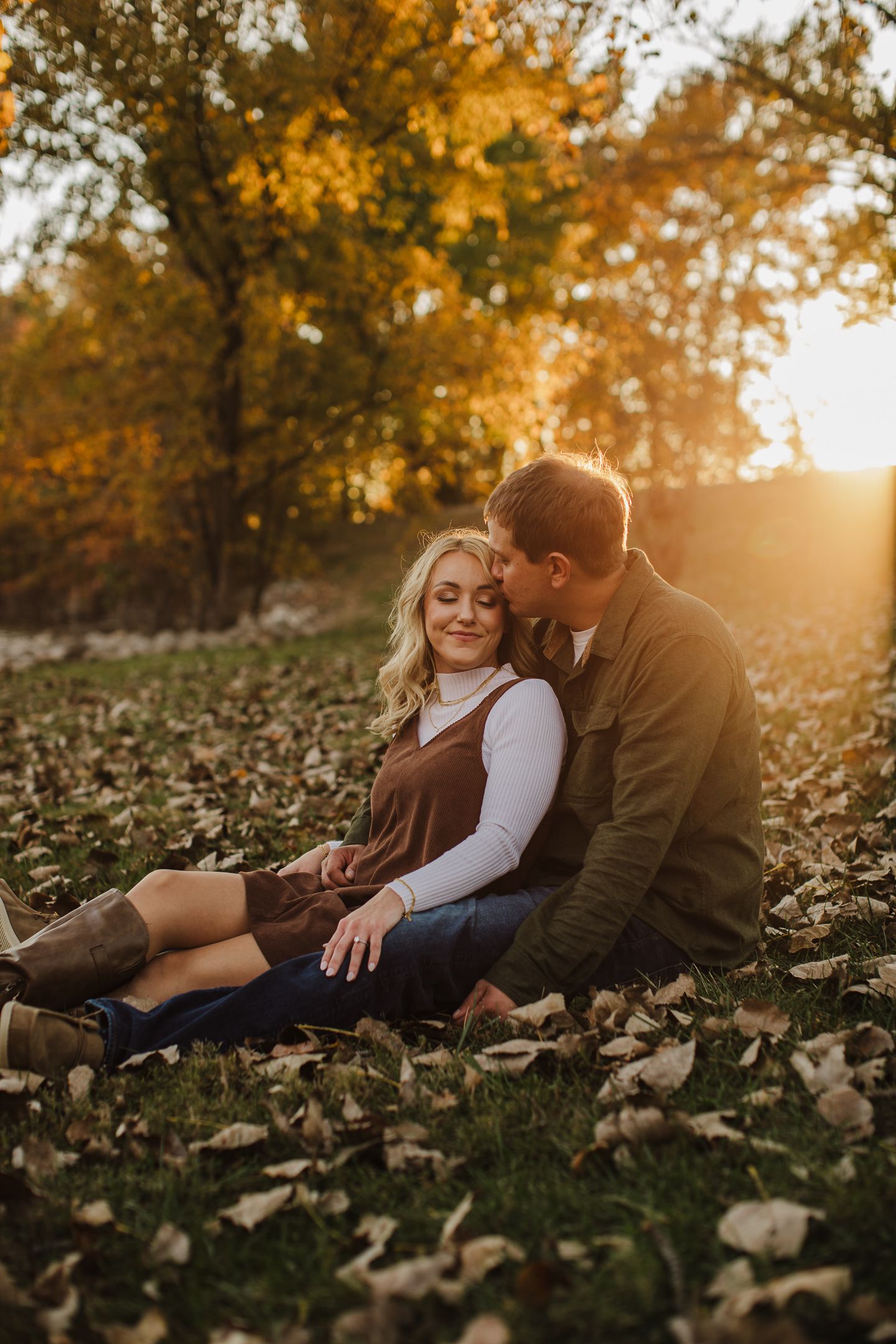 A couple shares an intimate moment while lying in autumn leaves at sunset.