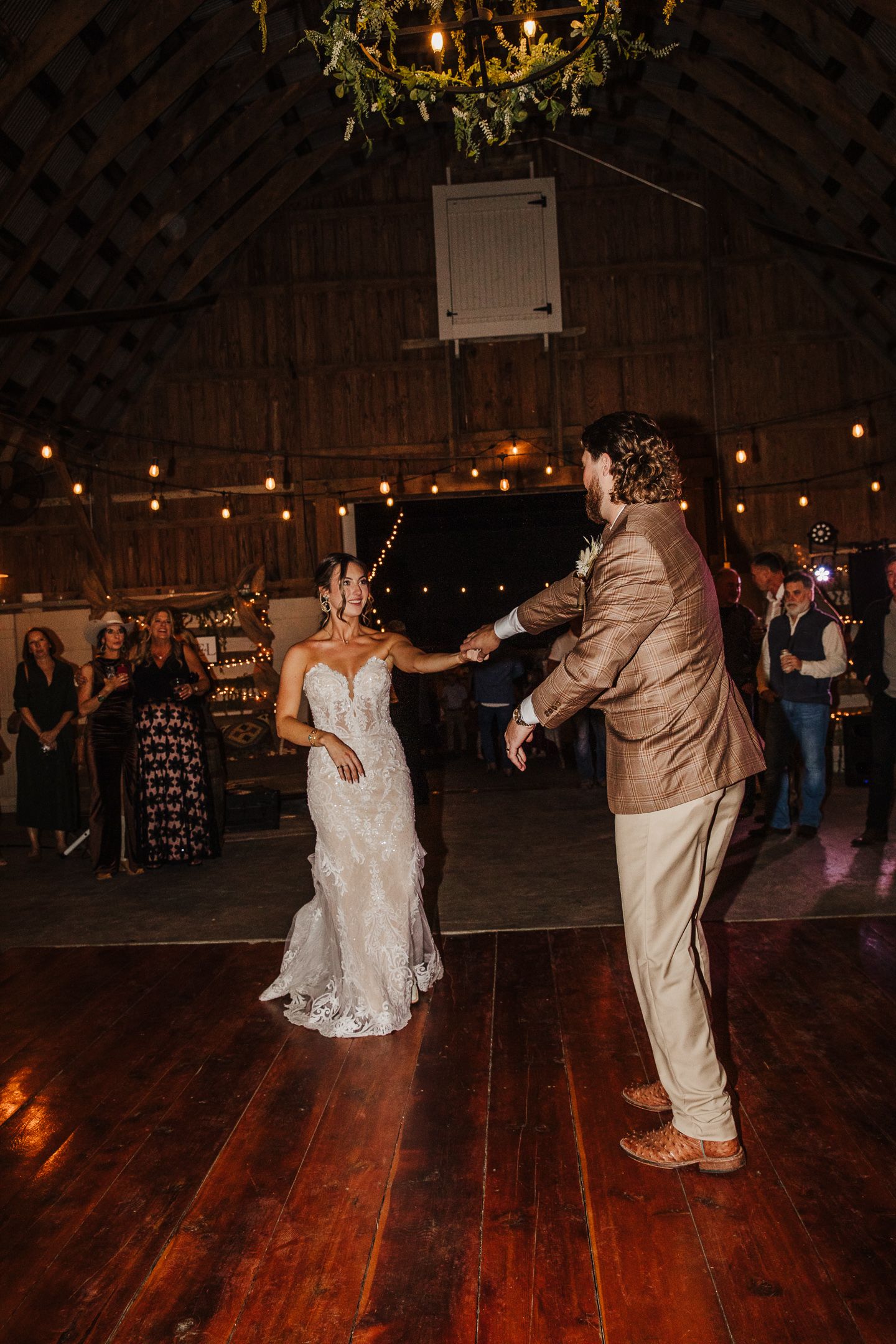 Wedding reception dancing in a rustic barn venue with string lights overhead.