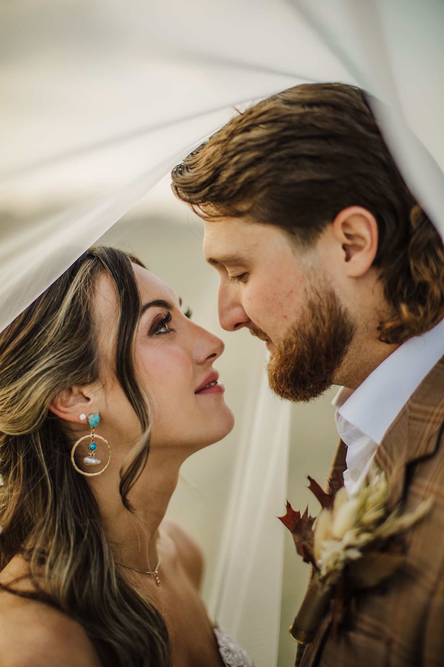 A romantic close-up moment between a couple with soft white fabric in the background.