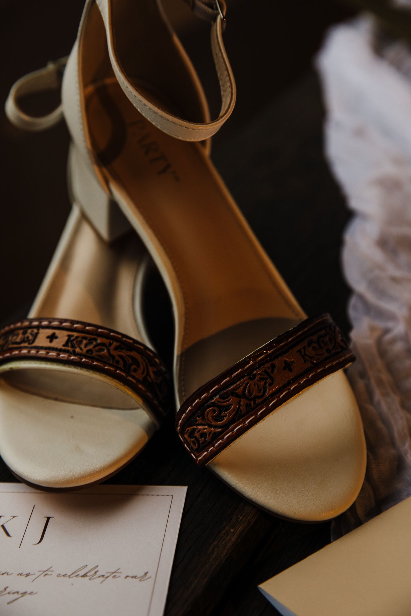 Elegant bridal sandals with ornate brown detailing and wedding stationery in soft lighting.