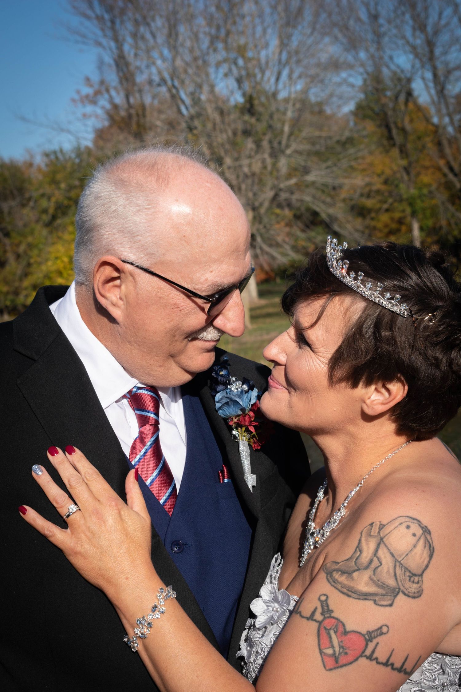 Bride and groom sharing an intimate moment outdoors, bride wearing tiara and showing tattoo.