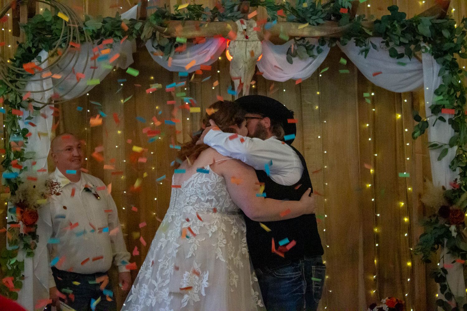 Bride and groom sharing first kiss under colorful confetti at wedding ceremony.