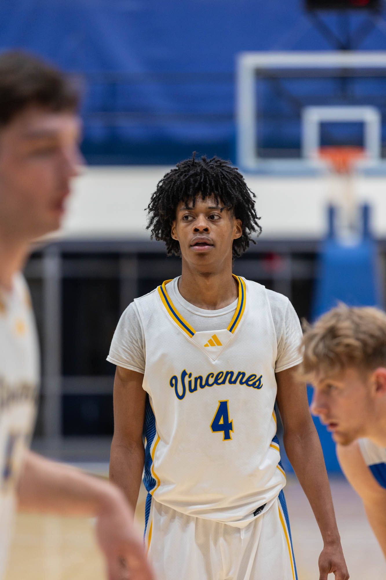 Vincennes University basketball player number 4 with dreadlocks stands on court during college game.