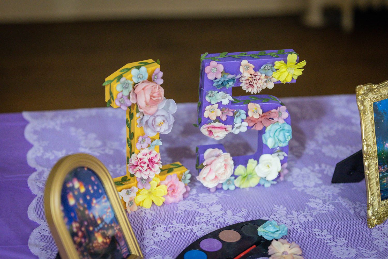 Floral decorated number 15 centerpiece on purple lace tablecloth for a quinceañera celebration.