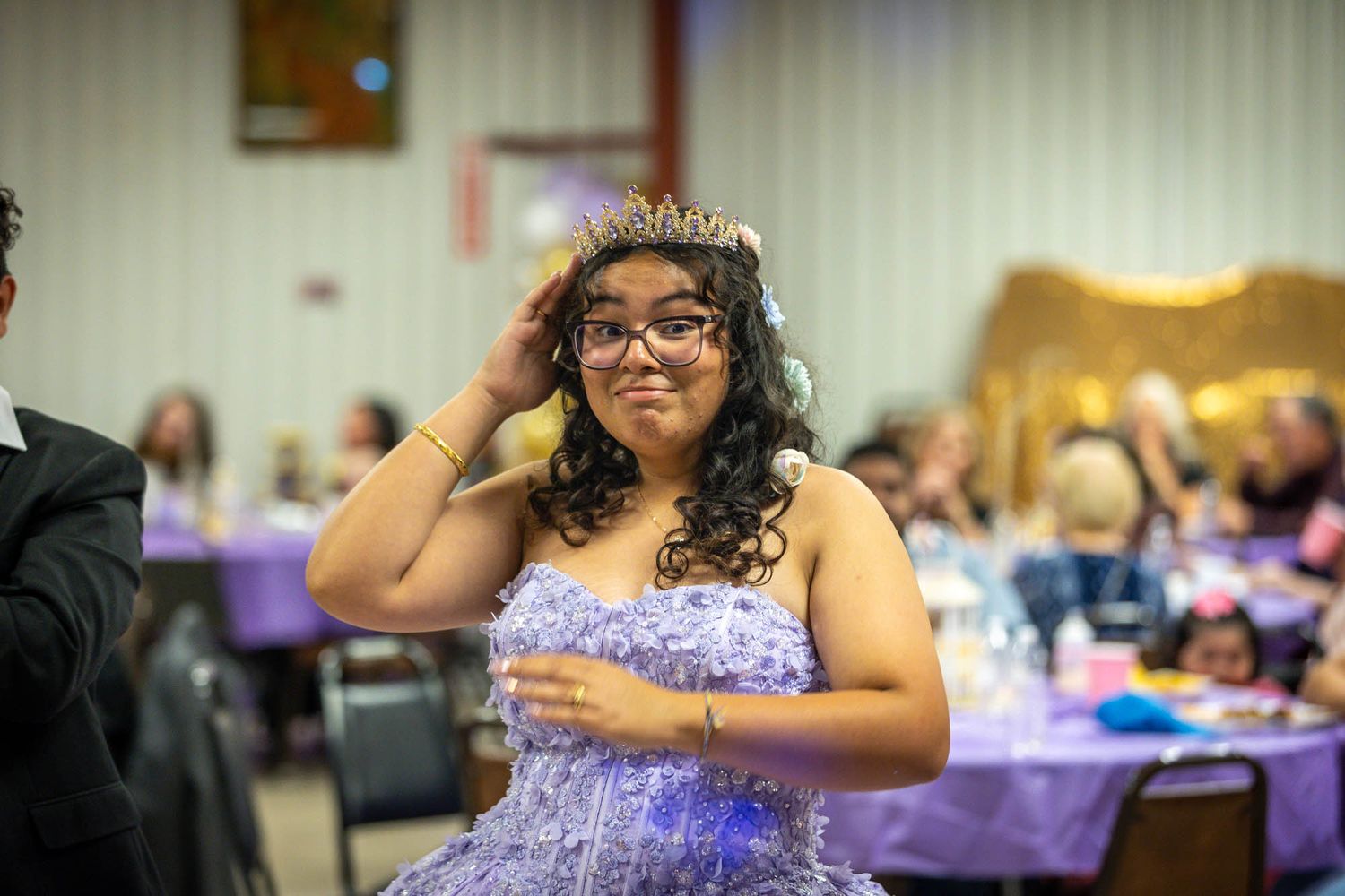 Young Quinceañera girl in purple gown adjusting her tiara crown at her celebration party.