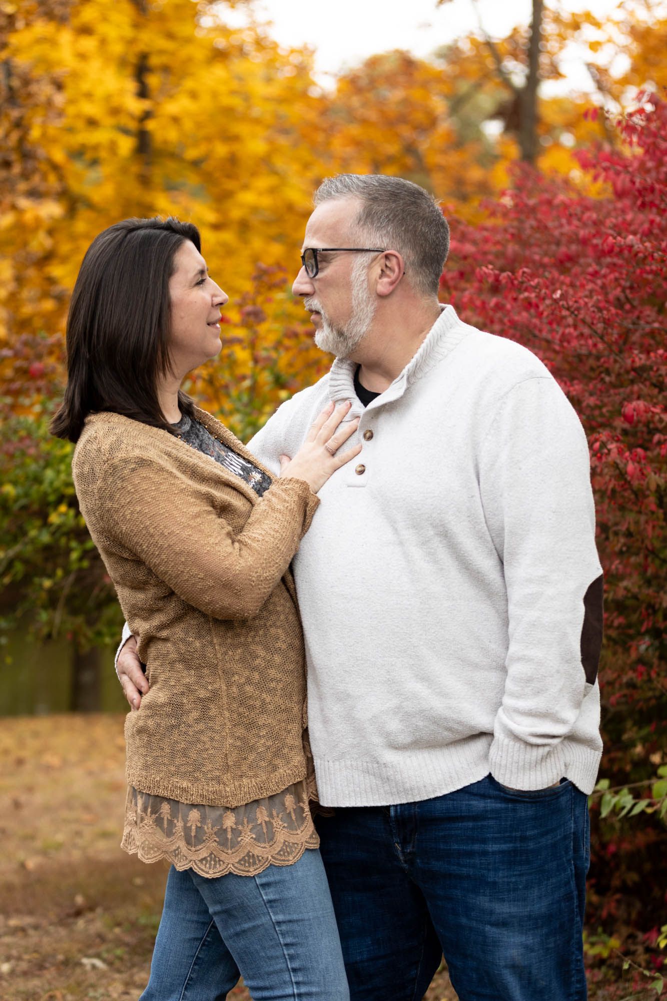 Couple sharing a tender moment together surrounded by vibrant red and yellow autumn foliage.