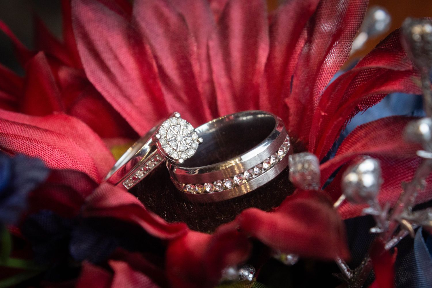 Diamond engagement ring and wedding bands displayed on red flower petals in bridal bouquet.
