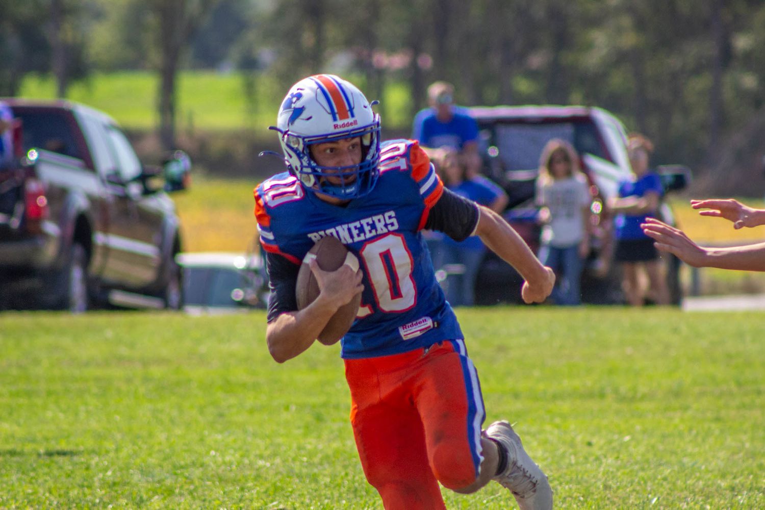 High school football player number 10 in blue and orange Pioneers uniform runs with the ball during a game.