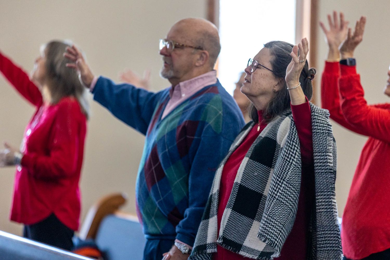 Couple raising hands in worship during a church service wearing colorful attire.