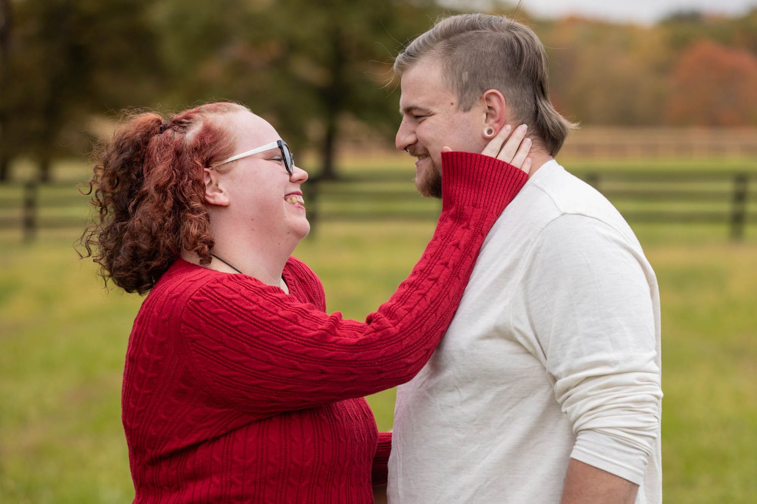 Couple gazes lovingly at each other during fall outdoor engagement photo session in open field.
