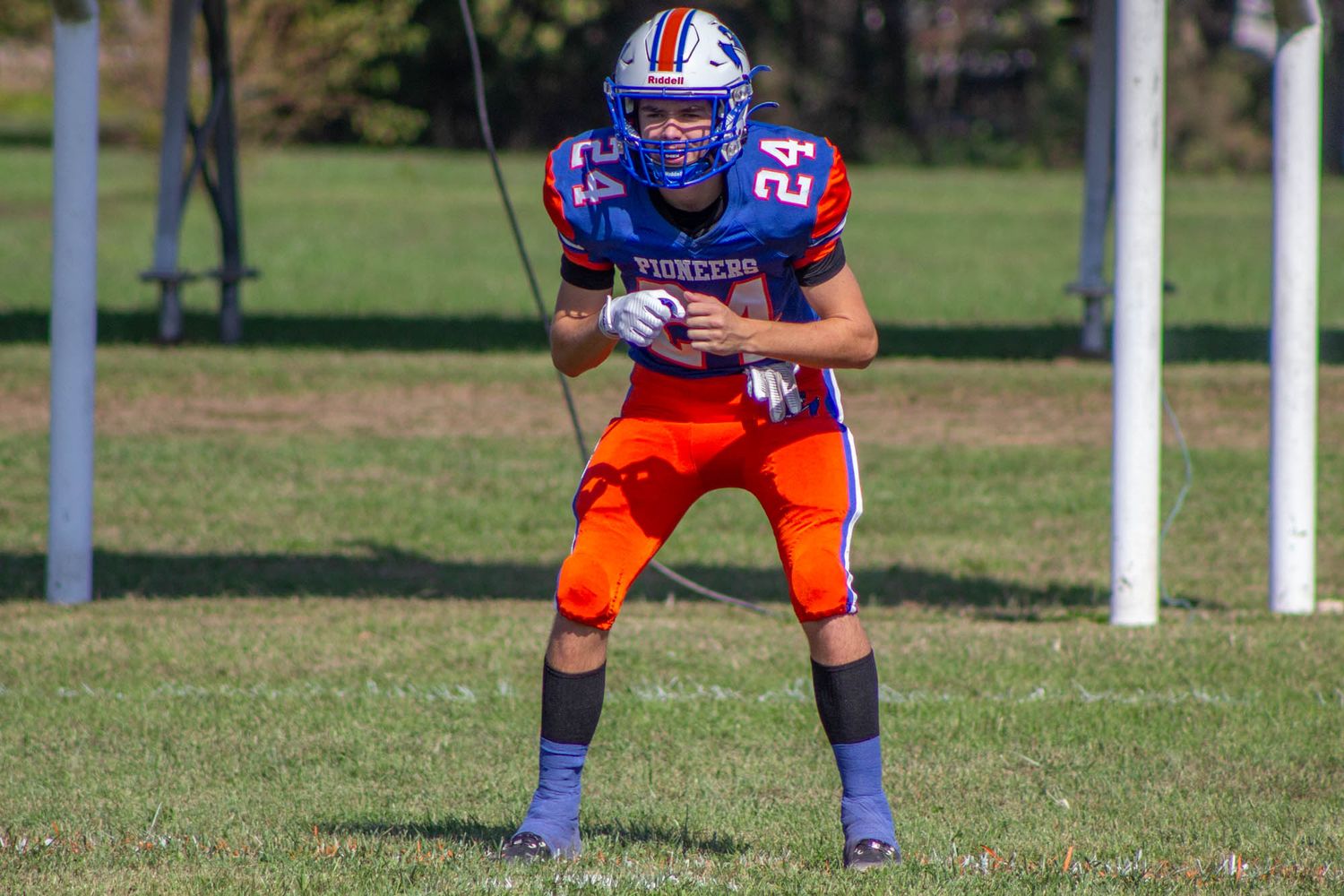 Youth football player #24 in blue and orange Pioneers uniform stands ready on the field.