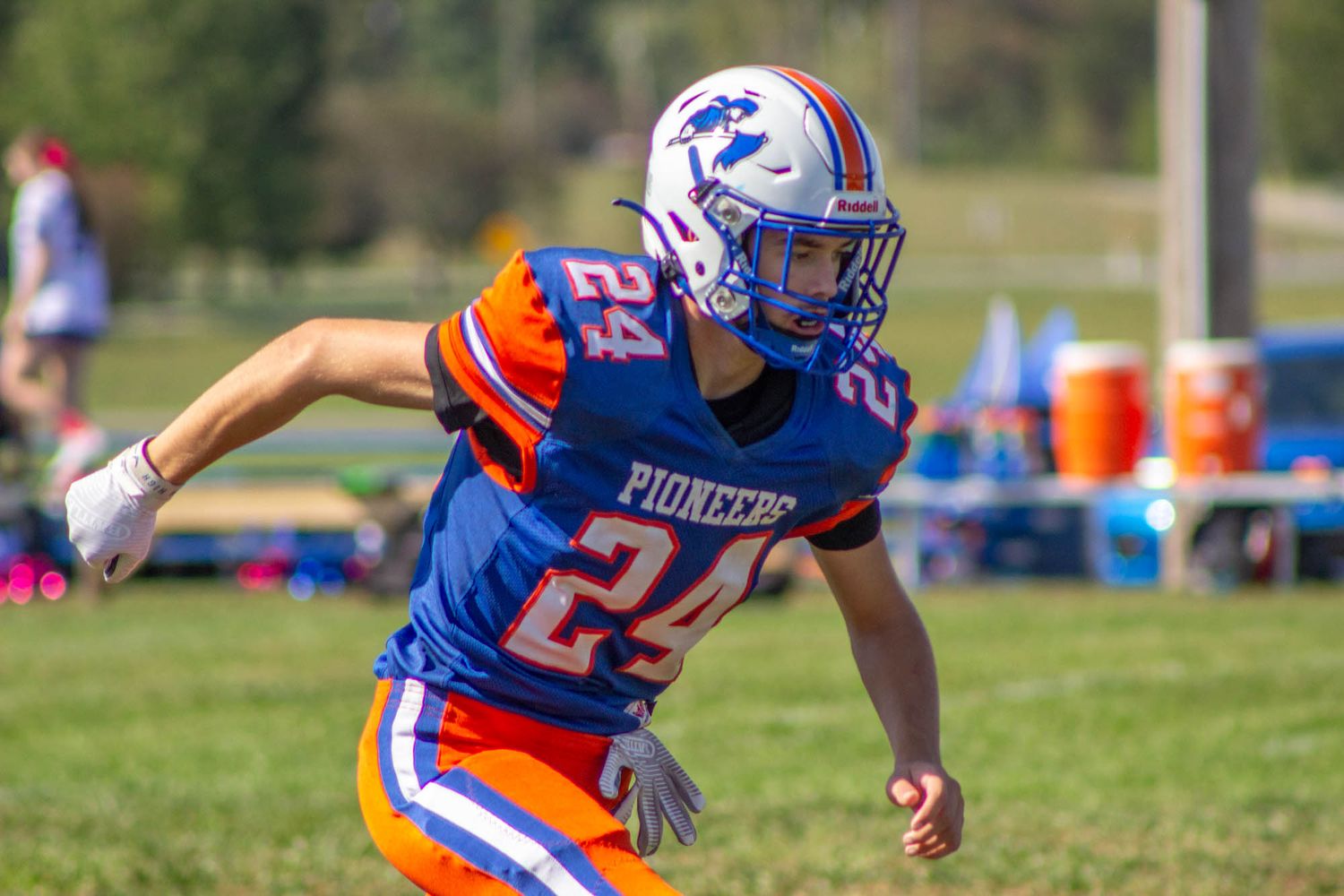 Pioneers youth football player #24 runs in blue and orange uniform during an outdoor game.