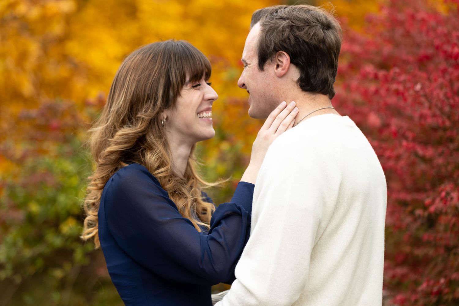 Romantic couple gazes at each other tenderly surrounded by vibrant red and yellow fall leaves.