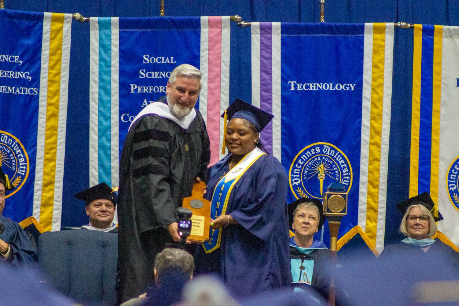 University official presents award to graduating student on stage during commencement ceremony.