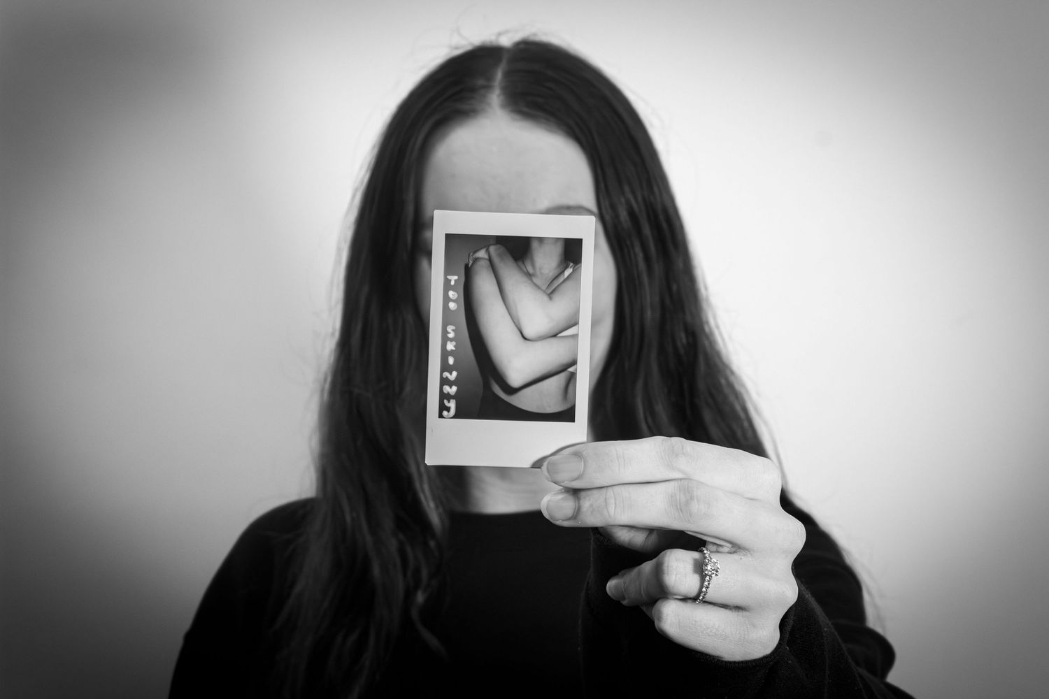 Black and white photo of a woman holding a Polaroid picture in front of her face.
