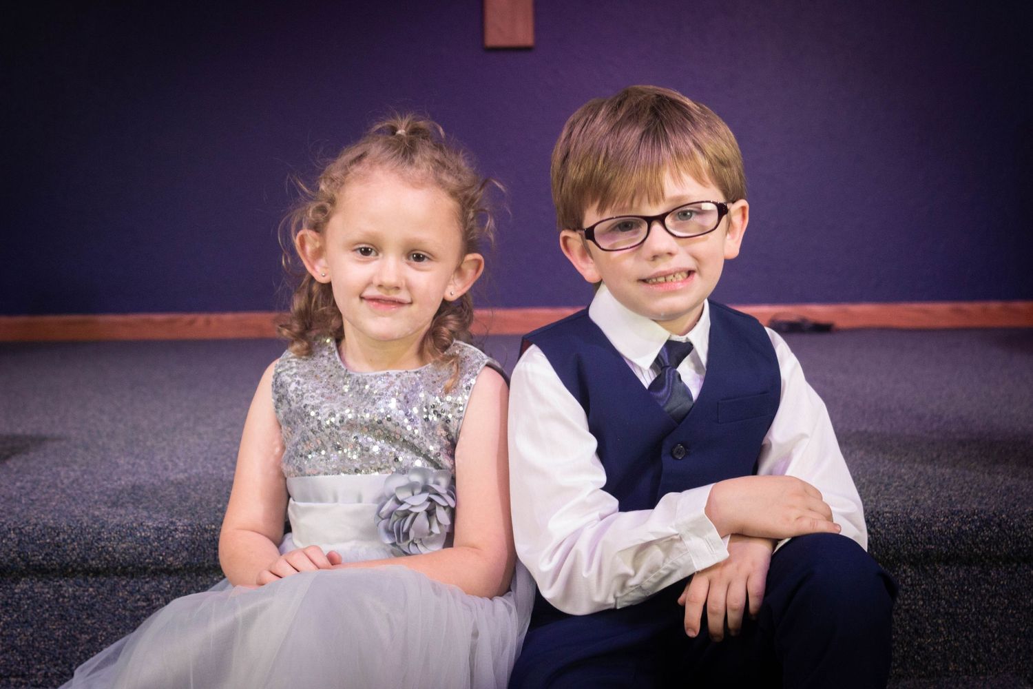 Young girl in silver dress and boy in suit sitting together at wedding.