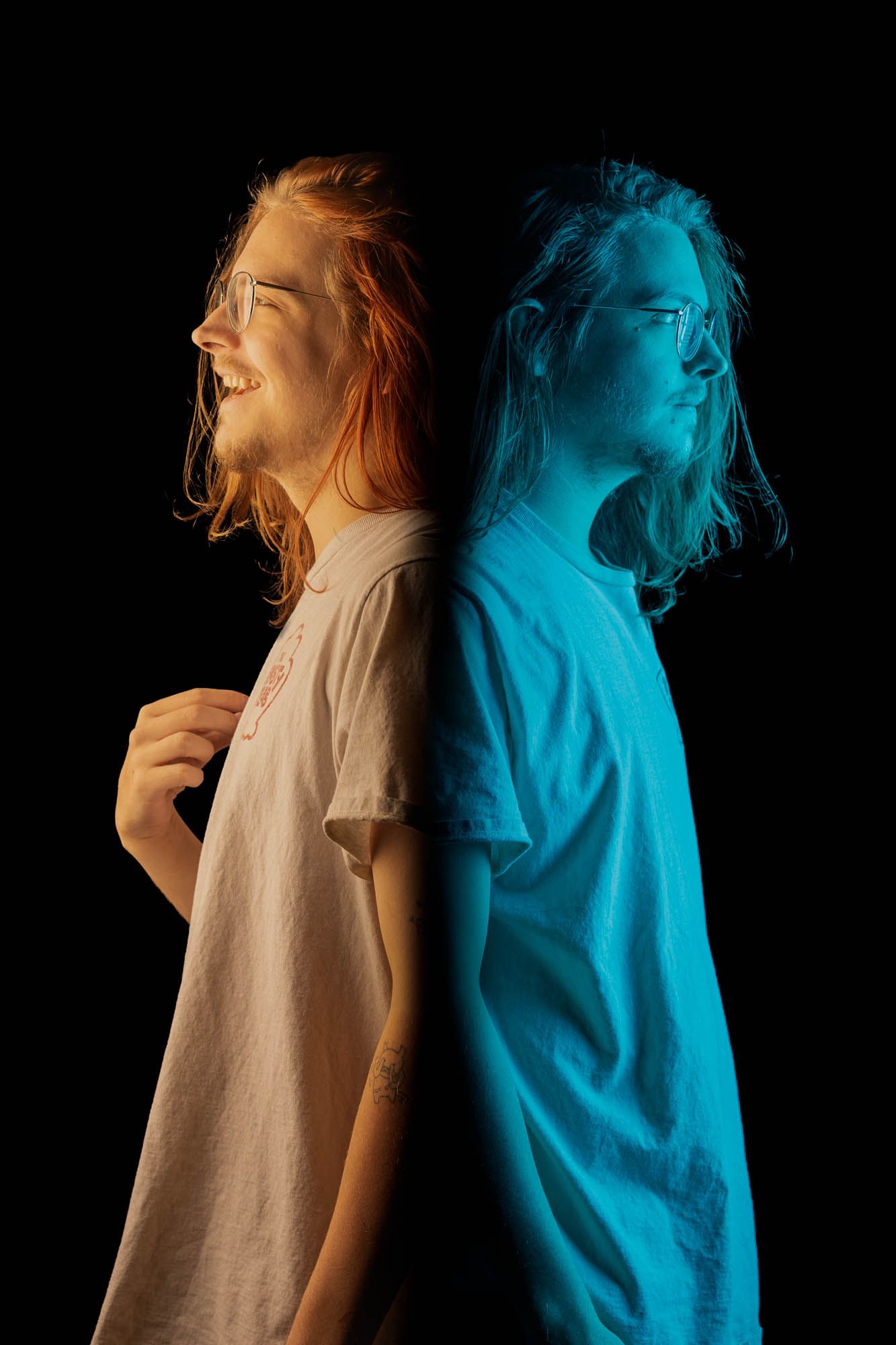 Long-haired person photographed back-to-back showing contrasting emotions in warm and cool blue lighting on black.