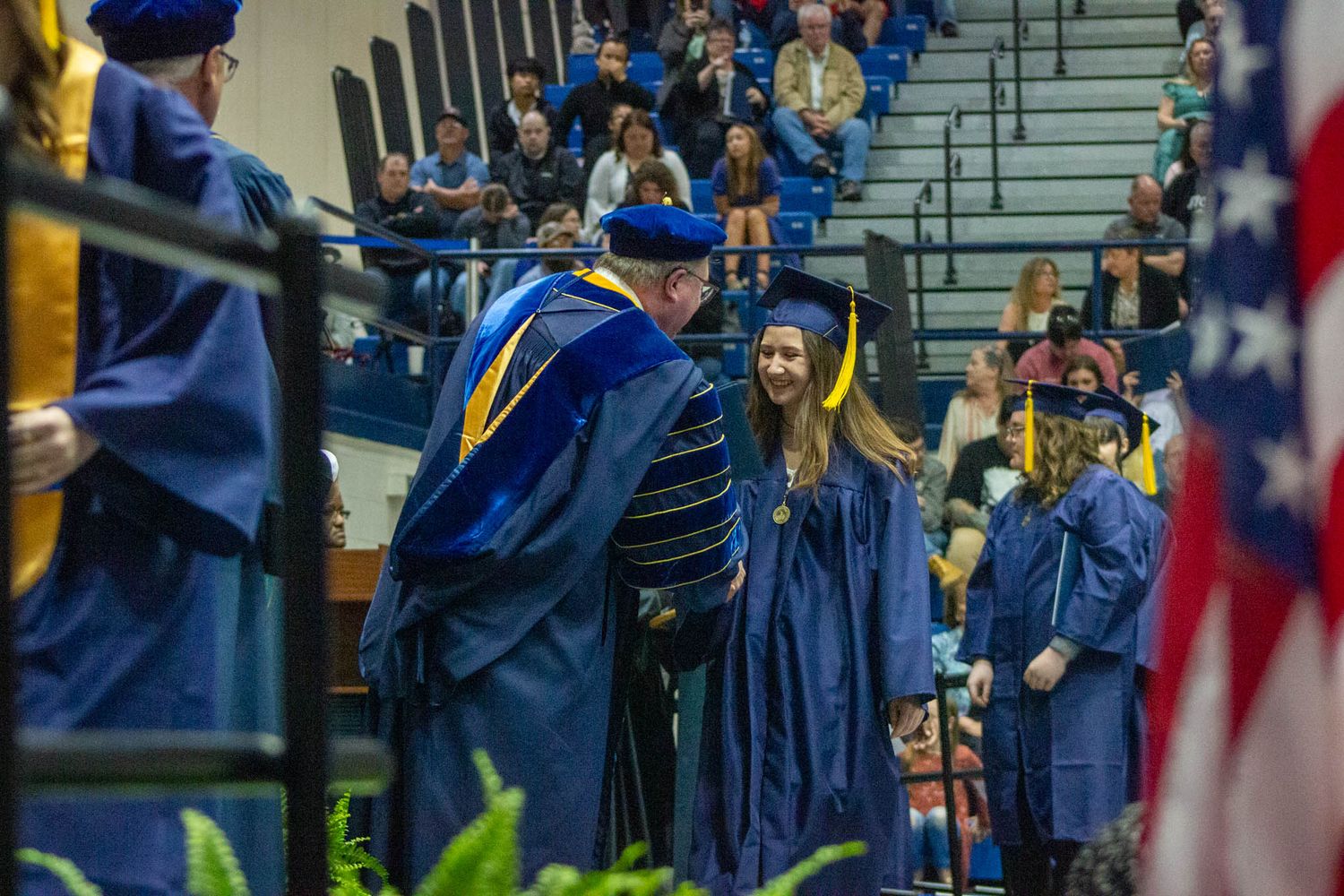A graduate receives congratulations from a faculty member in blue robes at a college commencement ceremony.