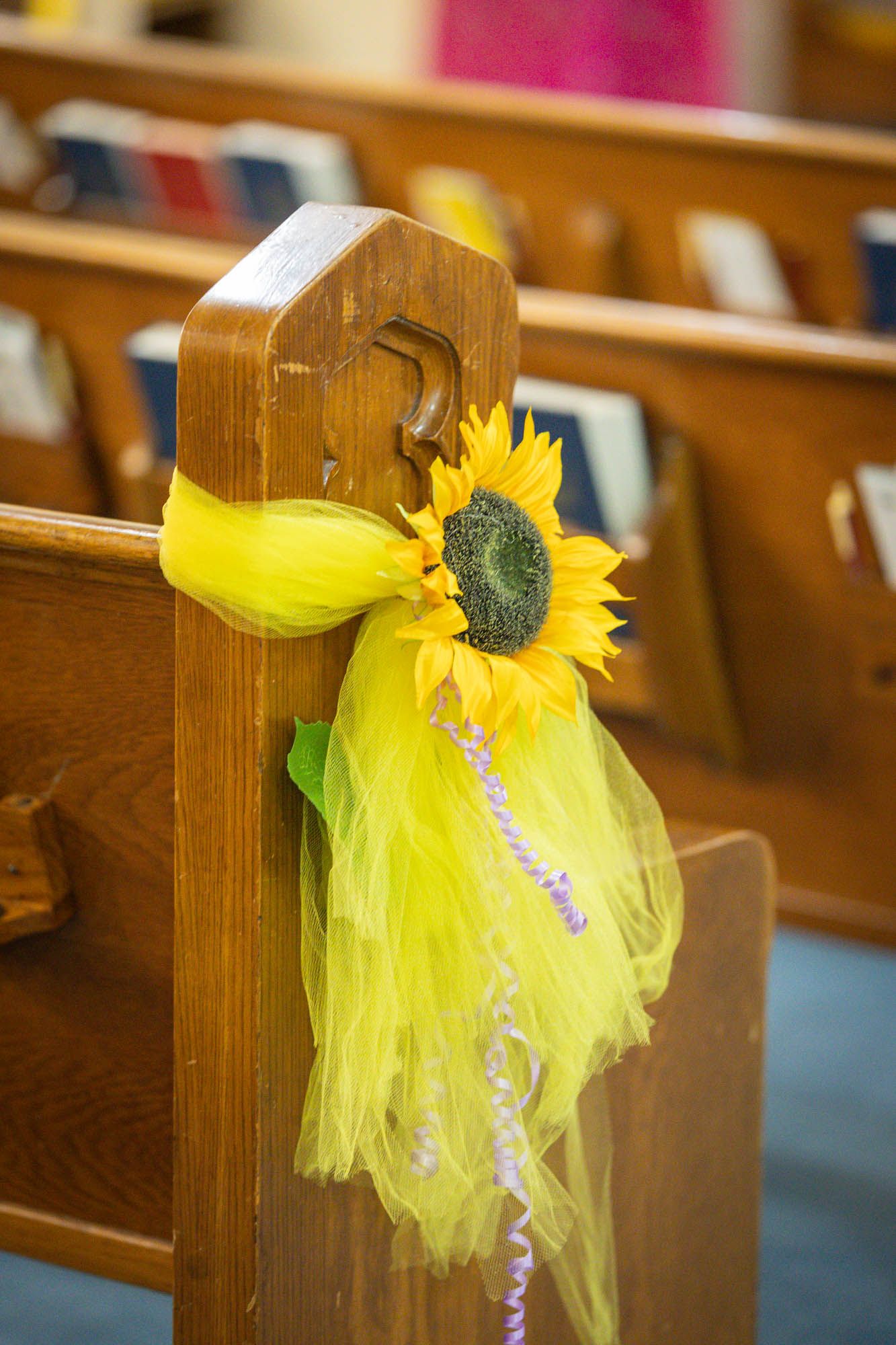 Yellow sunflower and tulle ribbon decoration on wooden church pew for a wedding ceremony.