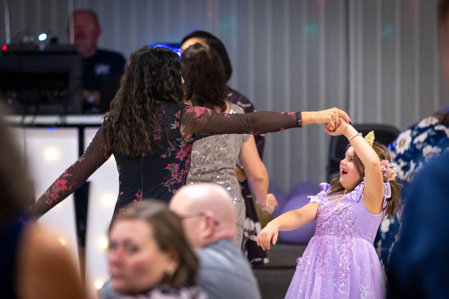 A young girl in a purple dress dances joyfully with adults at a quinceañera reception party celebration.