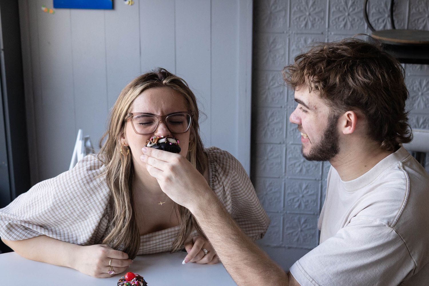 Young couple sharing a sweet moment as man feeds woman a chocolate cupcake at a cafe table.