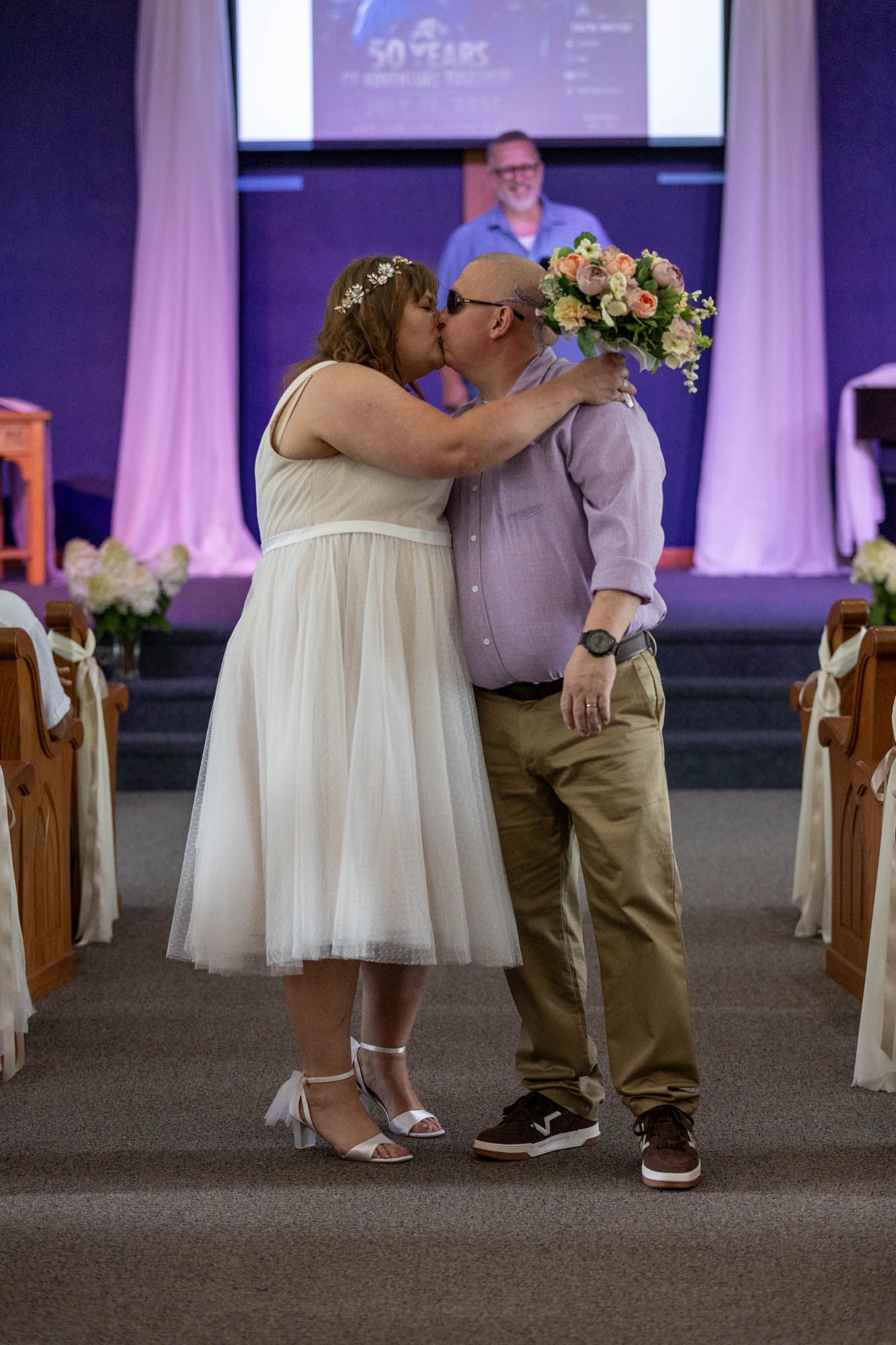 Bride and groom share first kiss at church altar while officiant stands behind them.