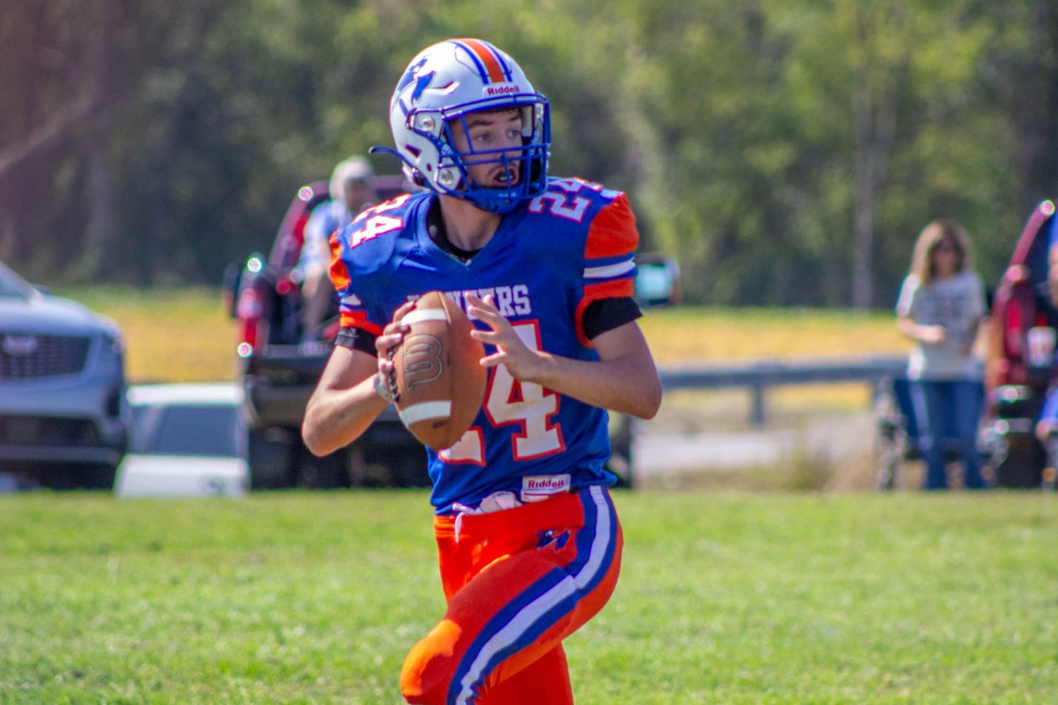 High school quarterback wearing number 24 in blue and orange uniform prepares to throw the football during a game.