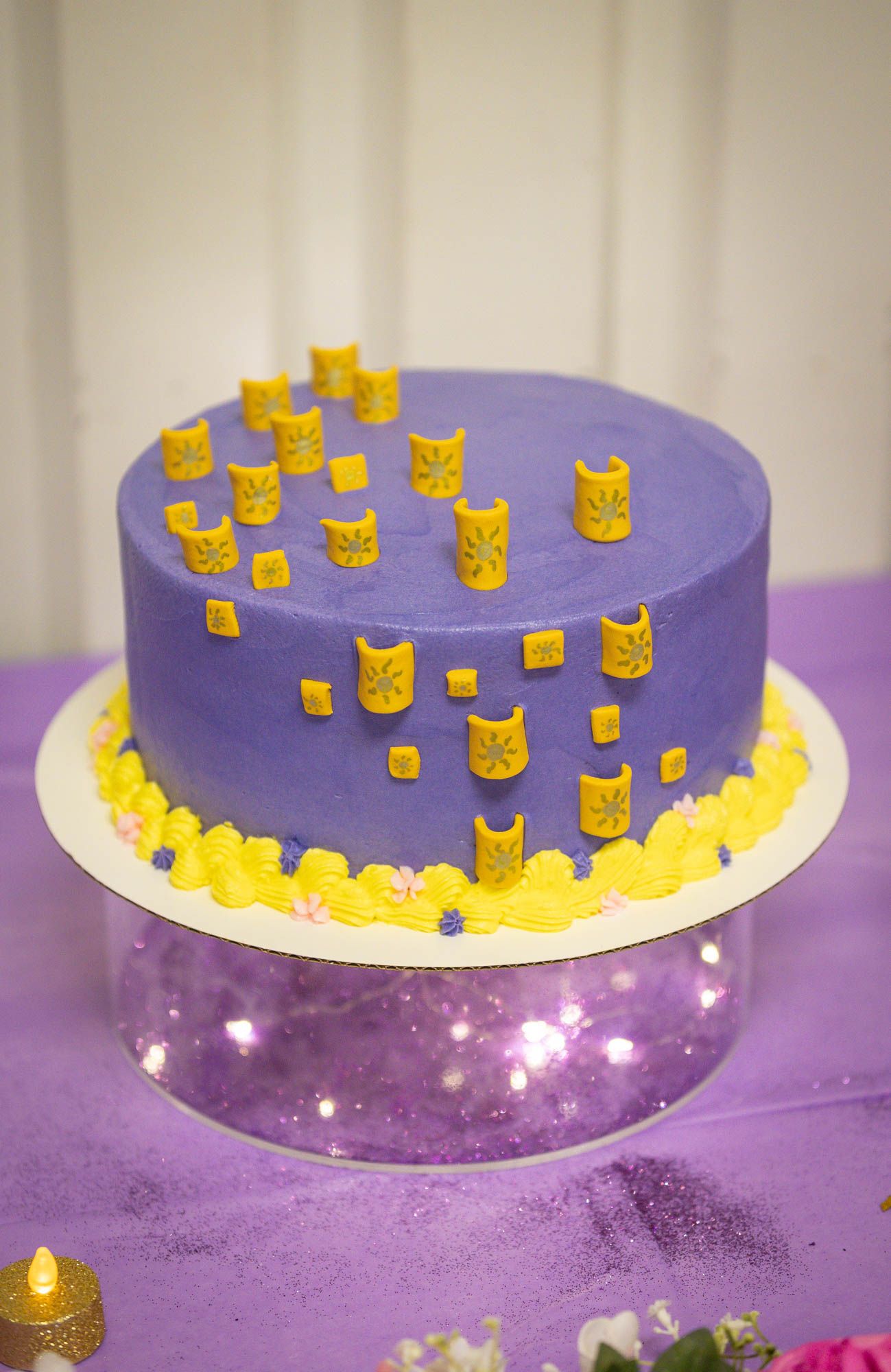A purple quinceañera cake decorated with golden lantern fondant pieces on a glittery cake stand.