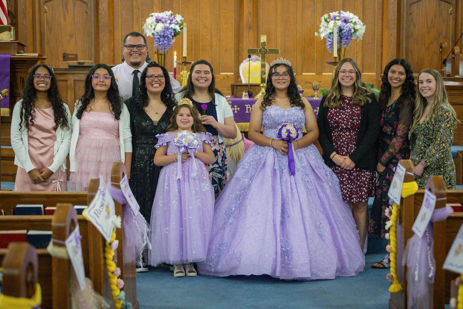 Quinceañera girl in lavender ball gown poses with her court and family inside a decorated church.