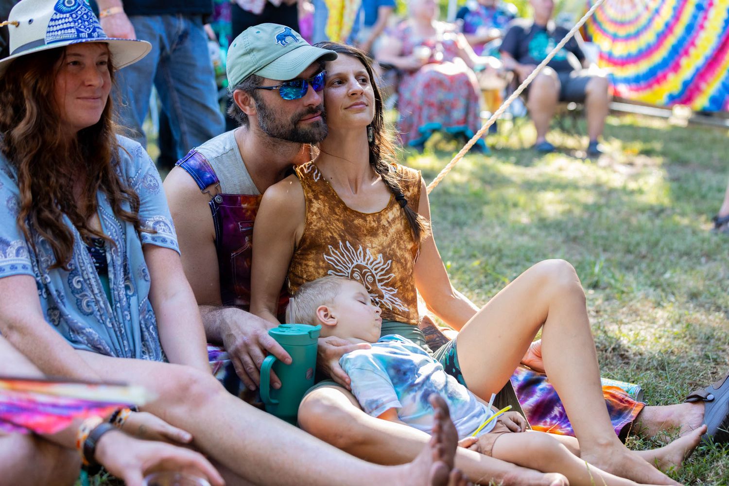 Couple relaxing on grass with baby at a colorful outdoor music festival.