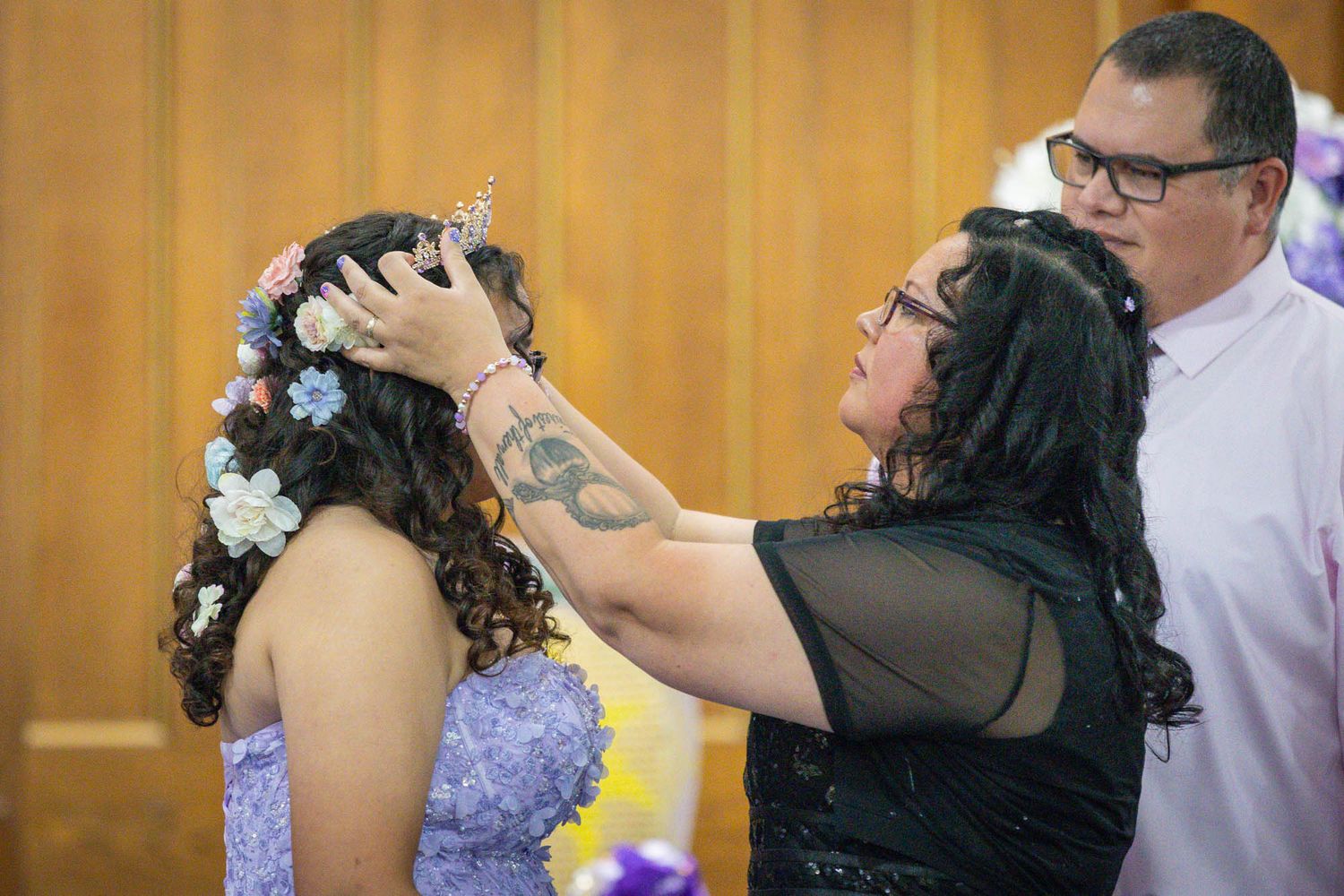 Woman placing floral crown on quinceañera girl in lavender dress during ceremony.