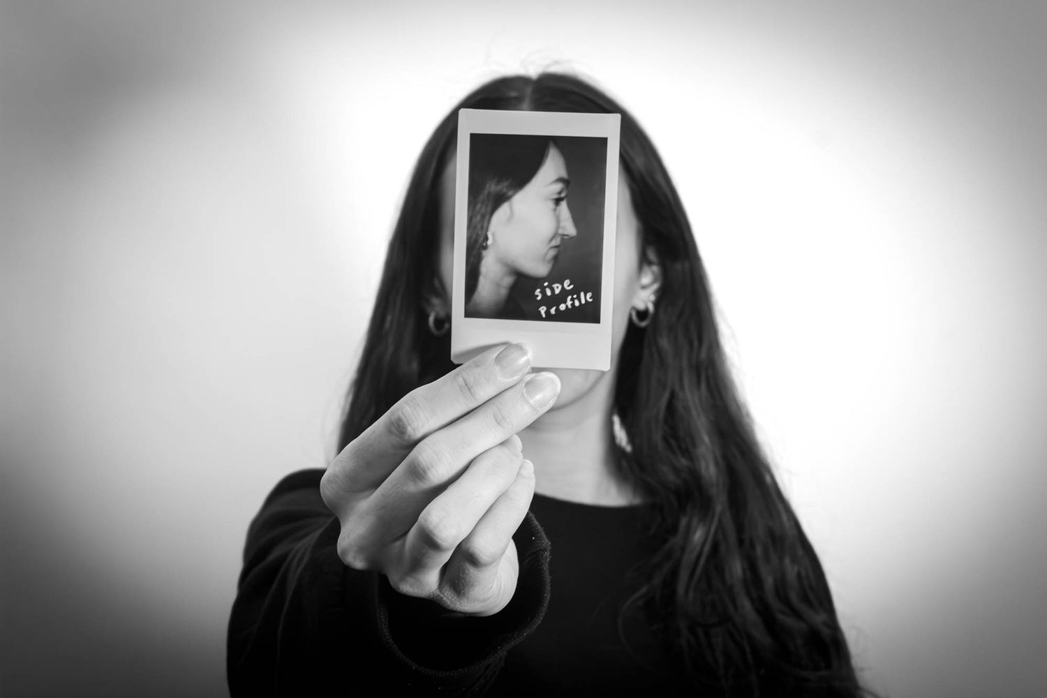 Woman holding a Polaroid photo in front of her face in black and white portrait photography.