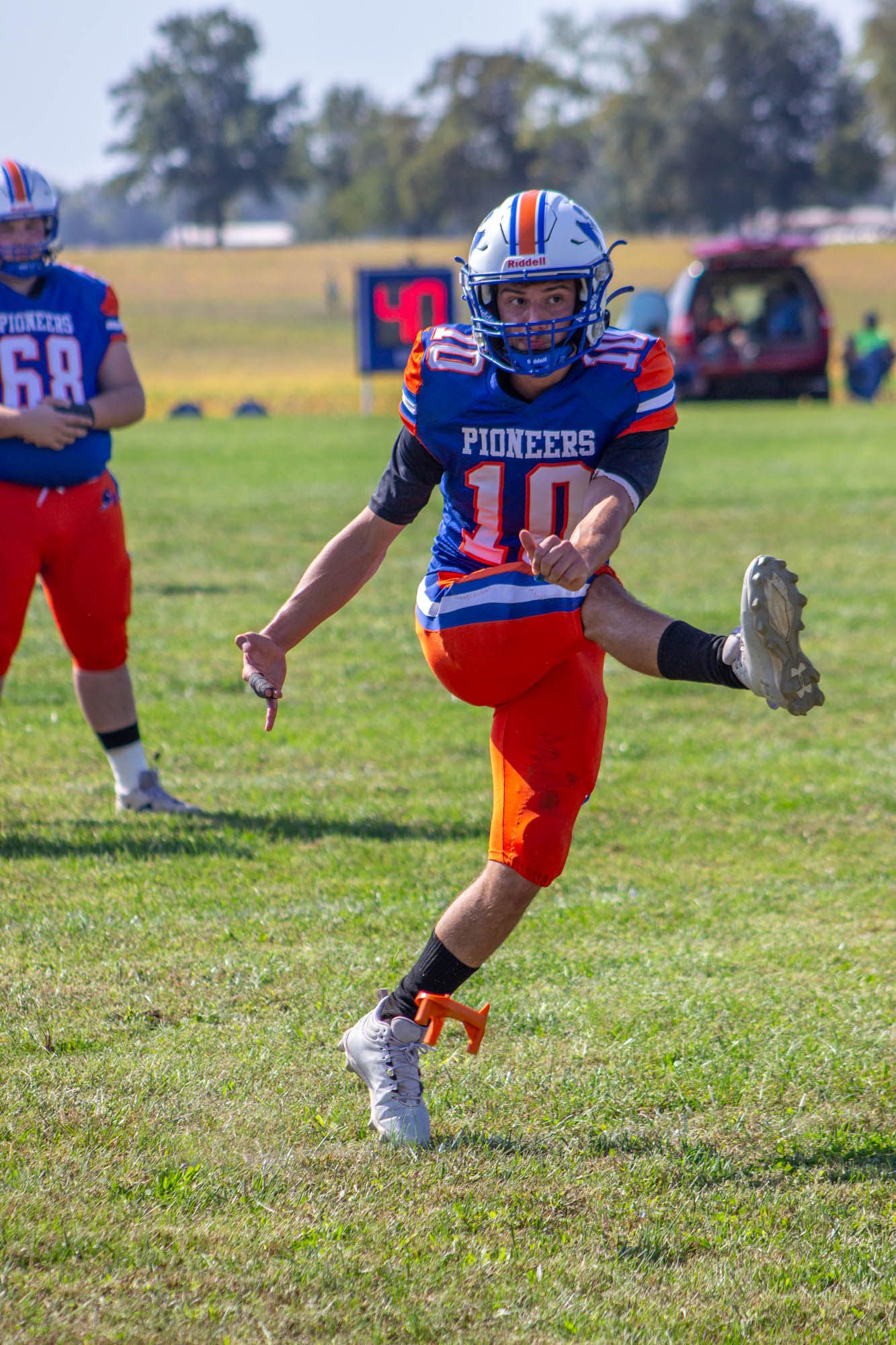Pioneers football player #10 executes a kick during a sunny outdoor youth football game.