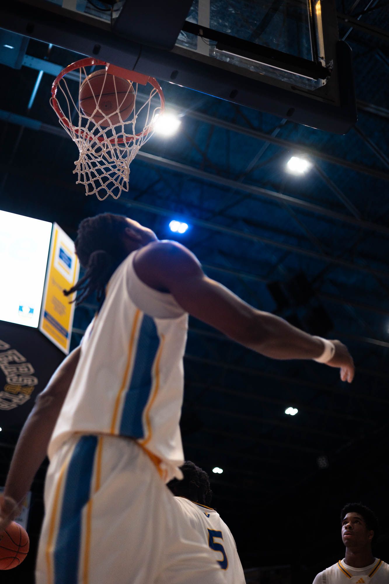 Basketball player in white Vincennes uniform reaches up toward the hoop during a game.
