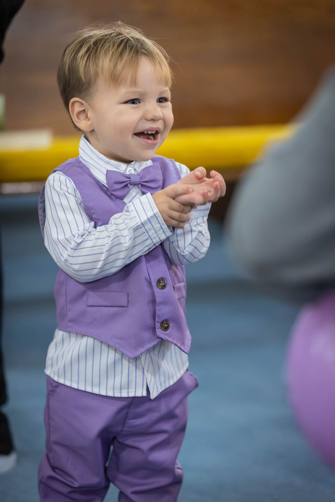 Adorable toddler boy in purple vest and bow tie clapping at a Quinceañera celebration.