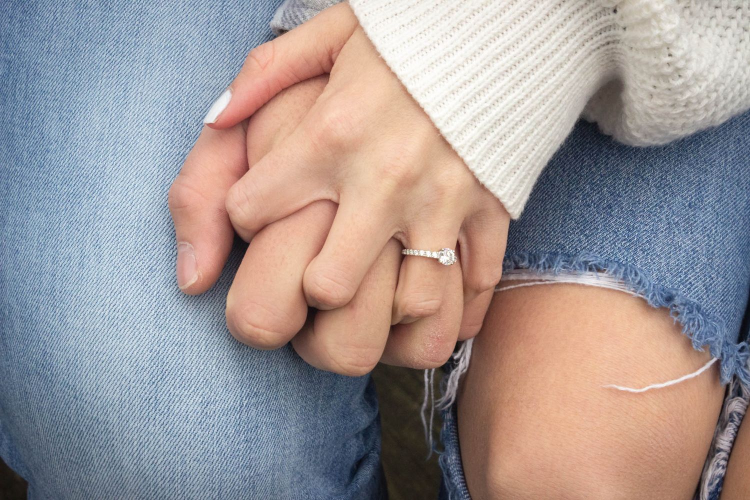 Close-up of couple holding hands, woman wearing diamond engagement ring on finger.