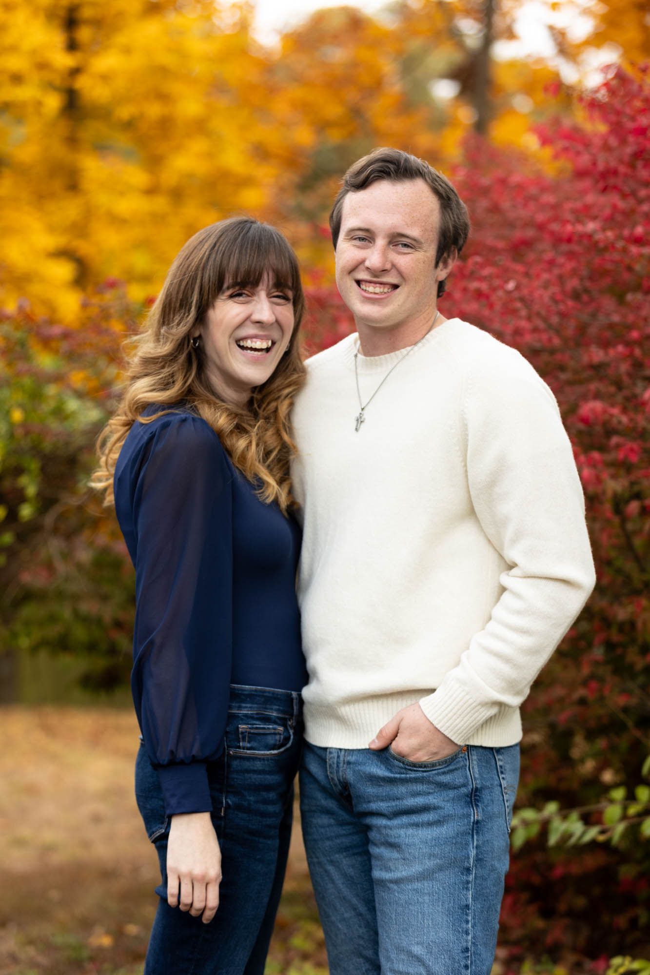 Happy couple laughing together outdoors surrounded by colorful red and yellow fall trees.