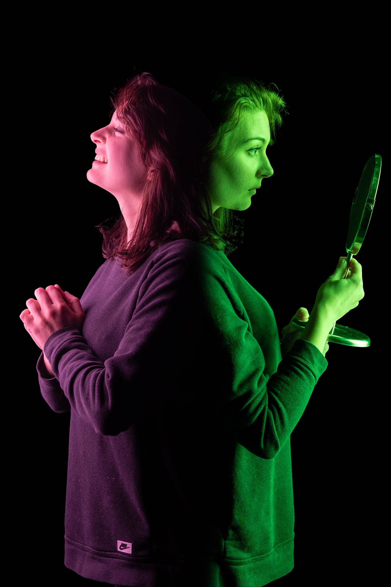 Woman photographed back-to-back in pink and green light, one side joyful, other holding mirror self-reflecting.
