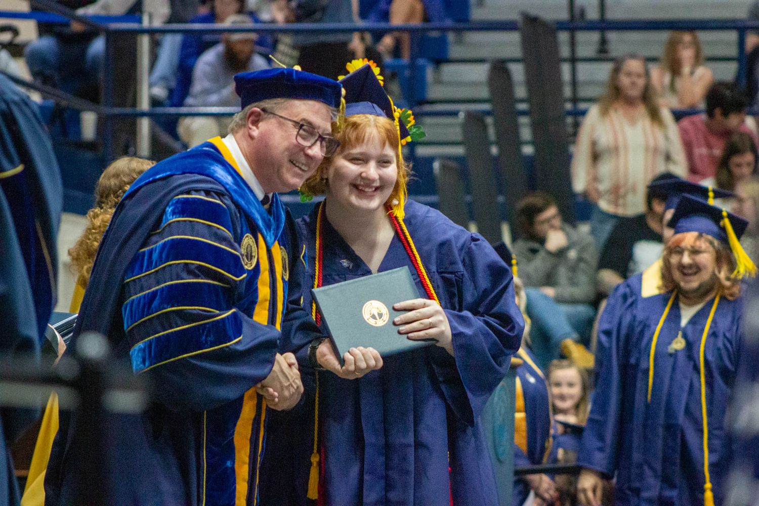 A smiling graduate poses with a professor in blue academic regalia during a college graduation ceremony.
