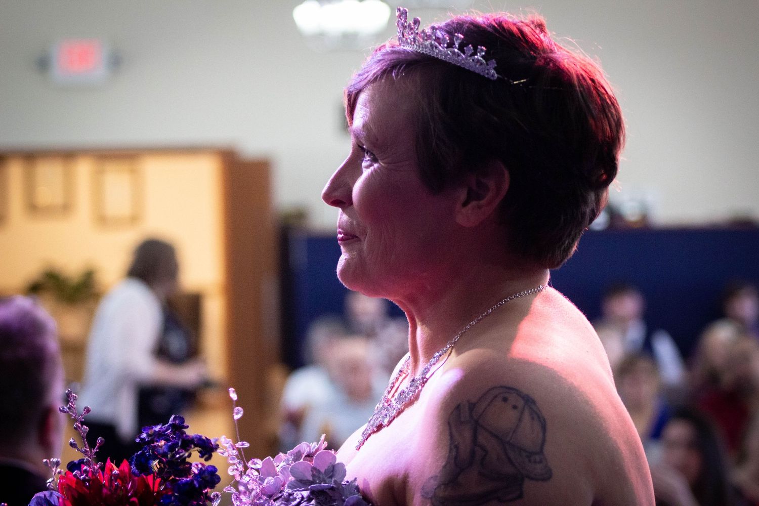 Bride wearing tiara and holding colorful bouquet at indoor wedding ceremony.
