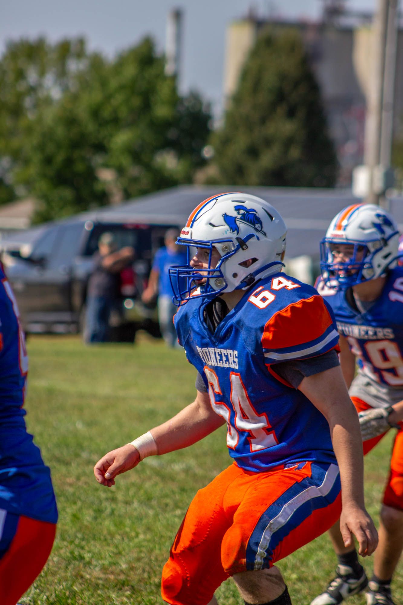 Youth football player number 64 in blue and orange uniform running on field during game.