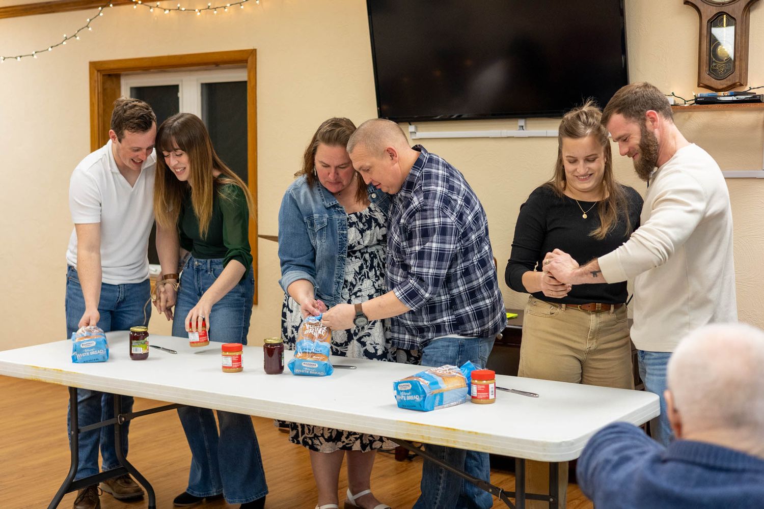 A group of six adults gather around a table participating in a fun activity at an indoor event.