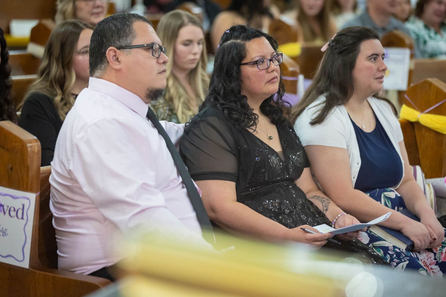 Family seated in church pews during a quinceañera ceremony, man in pink shirt beside two women.