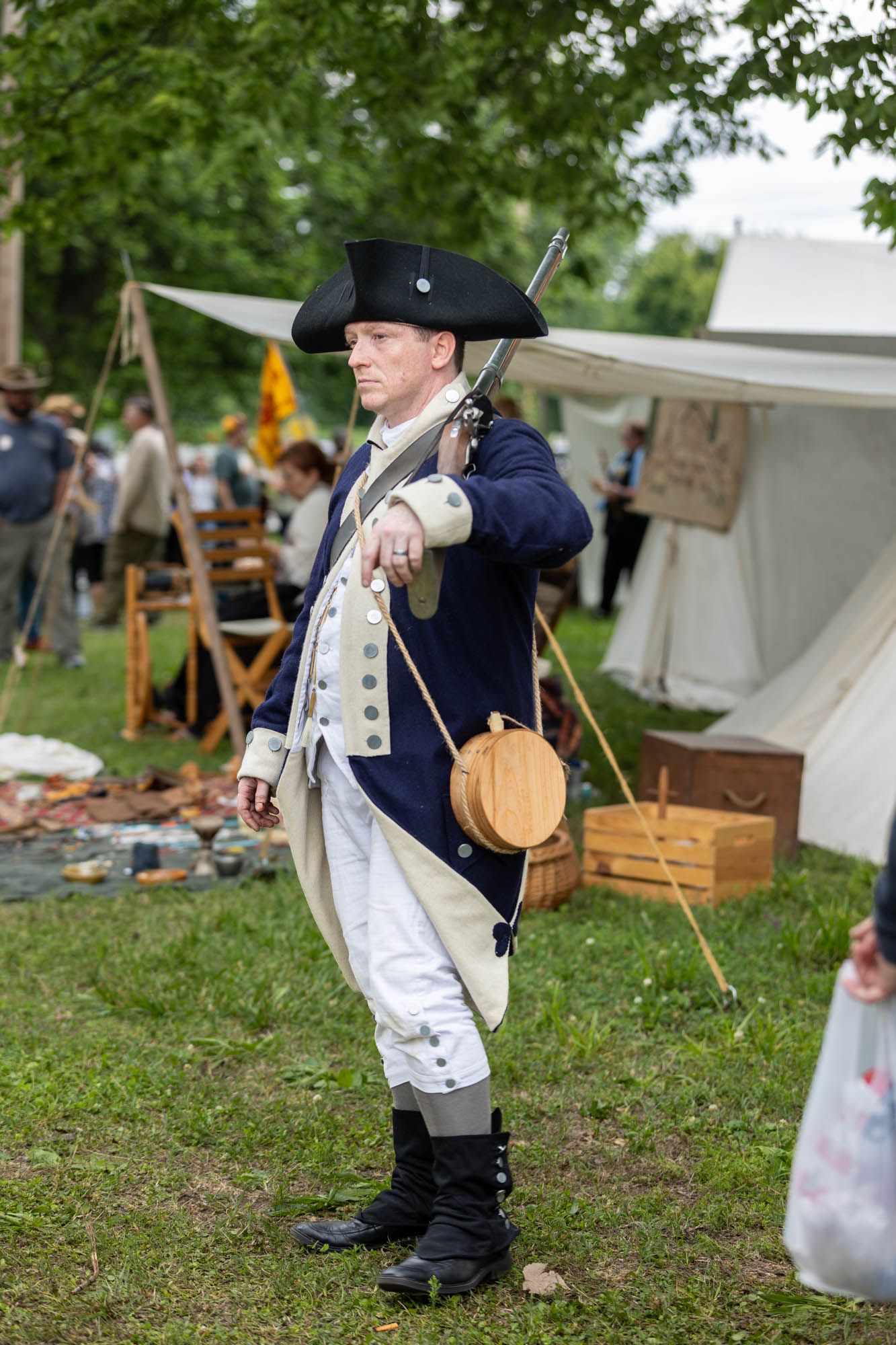 Man in Colonial American Revolutionary War soldier costume at historical reenactment event outdoors.